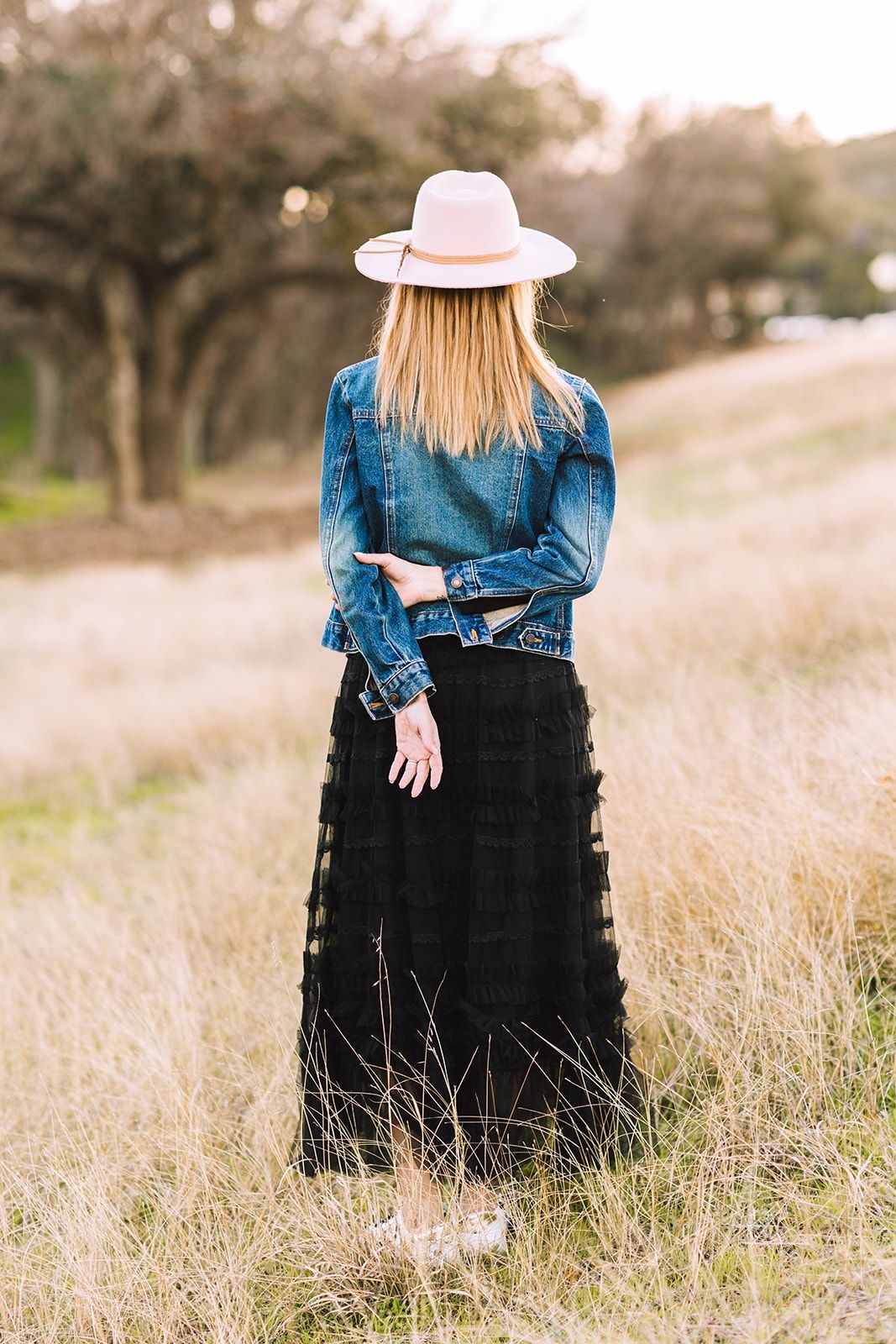 Confident life coach immersed in nature, standing poised with back to the camera, symbolizing readiness to embrace life's challenges. Ready to tackle goal setting, problem-solving, and happiness pursuits, fostering decreased stress, heightened productivity, and overall life maximization.